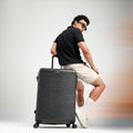 Charcoal grey hard-shell check-in suitcase with textured surface, handle, and 8 wheels