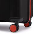 Close-up of hard-sided suitcase wheels and corner base, black shell with red wheel accents.
