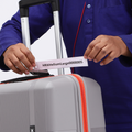 Hands holding a boarding tag on a grey suitcase; red zipper trim on edge