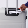 Medium check-in suitcase close-up of handle with attached label; PP shell in light gray.