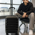 Black polypropylene cabin trolley standing near seated traveler with telescopic handle up