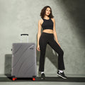 Grey hard-shell check-in suitcase with 8 wheels, curved ridges, and upright handle.