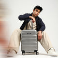 Silver hard-shell suitcase with telescopic handle and four wheels, carried by handle