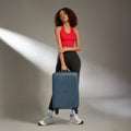 Teal-blue cabin suitcase with telescopic handle and four wheels, carried by traveler