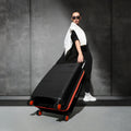 Black rolling suitcase with ribbed texture, orange wheels, and top handle