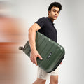 Green small cabin suitcase held by a person, upright carry with handle.