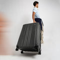 Traveler holding a hard-shell check-in suitcase with 8 wheels and telescopic handle