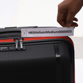 Medium check-in suitcase, black textured shell with red zipper trim, front close-up
