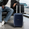 Navy cabin trolley with telescopic handle and four wheels beside a seated traveler.