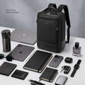 Black backpack with front tech pocket, displayed with laptop and small accessories.