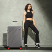 Grey hard-shell check-in suitcase with 8 wheels, curved ridges, and upright handle.