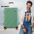 Green hard-shell check-in suitcase with 8 wheels and upright handle, next to traveler.