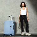 Light blue hard-shell spinner suitcase with telescopic handle, shown beside standing woman