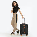 Black soft-sided spinner trolley held by a woman, with front pocket and orange accents