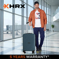 HRX medium polypropylene suitcase in dark teal, upright with 4 wheels indoors