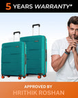 Pair of teal upright hard-shell suitcases with telescopic handles and orange wheels
