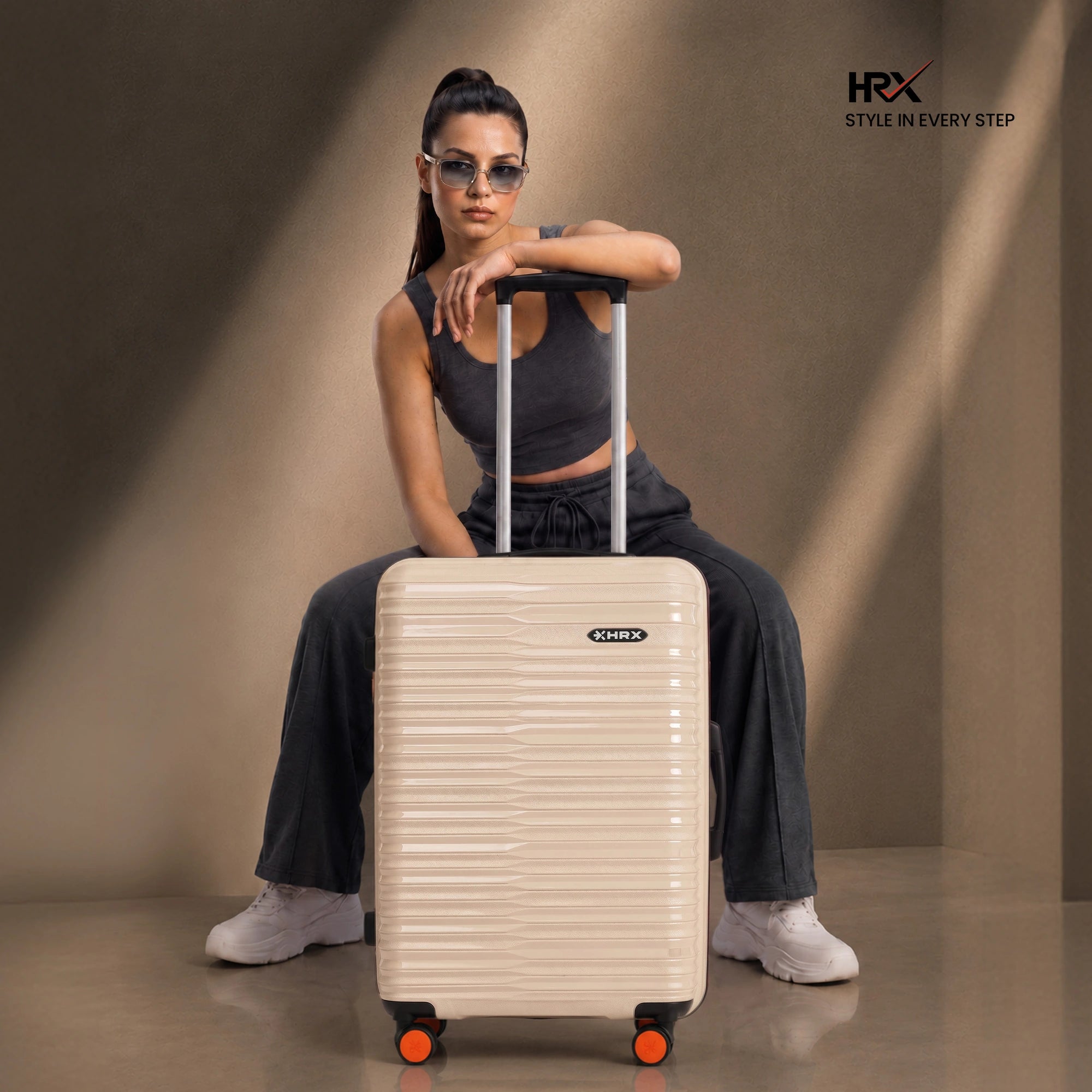 Beige medium check-in suitcase with upright handle, orange wheels, and textured shell.