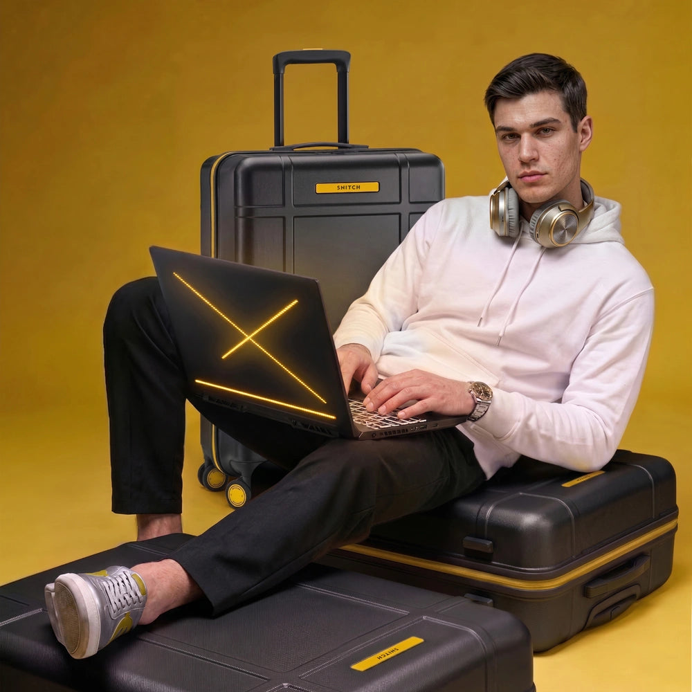 Black polycarbonate trolley suitcase with laptop on top; man seated beside it
