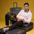 Black polycarbonate trolley suitcase with laptop on top; man seated beside it